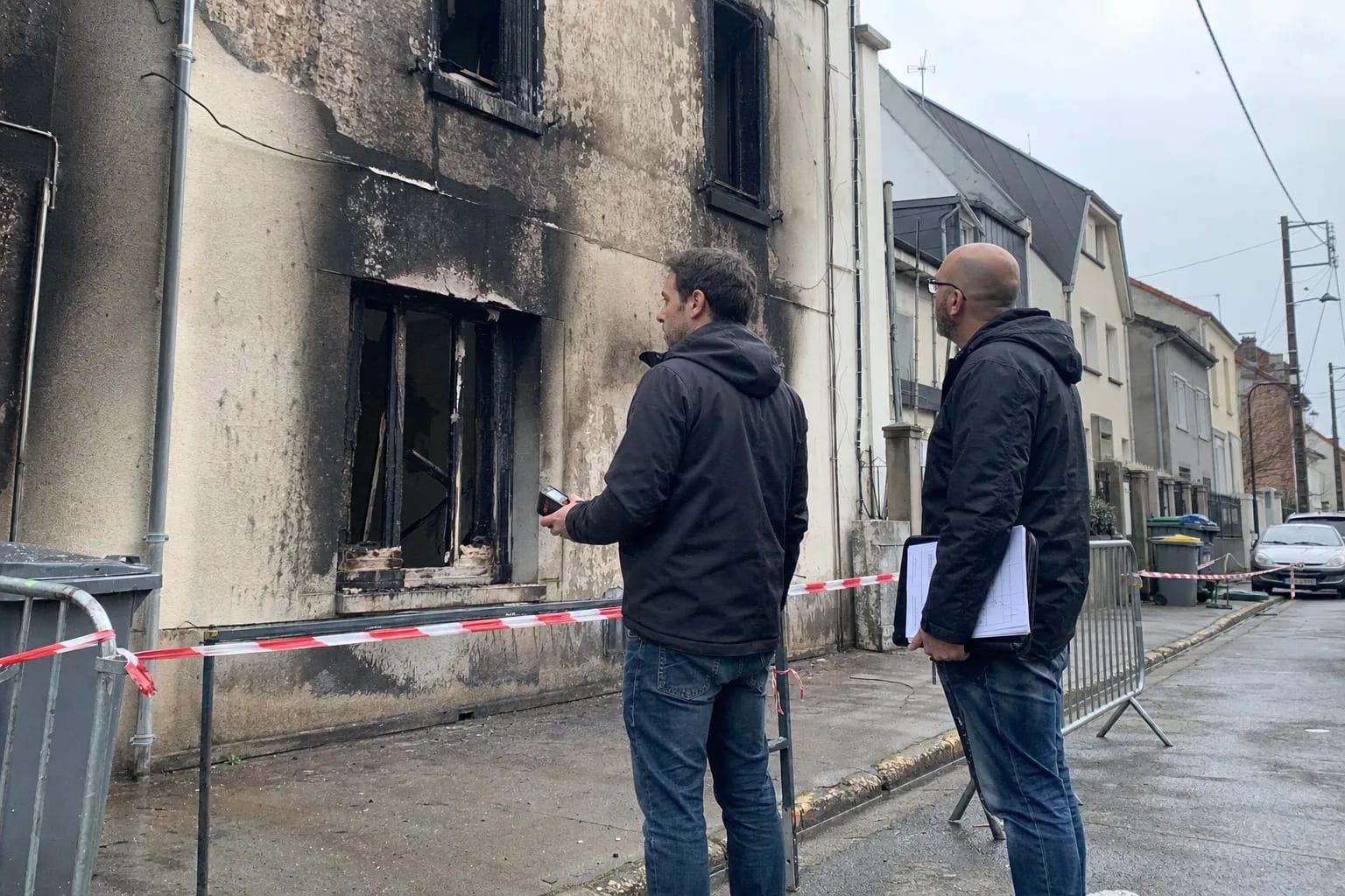 Deux experts comparant leurs relevés devant une façade sinistrée
