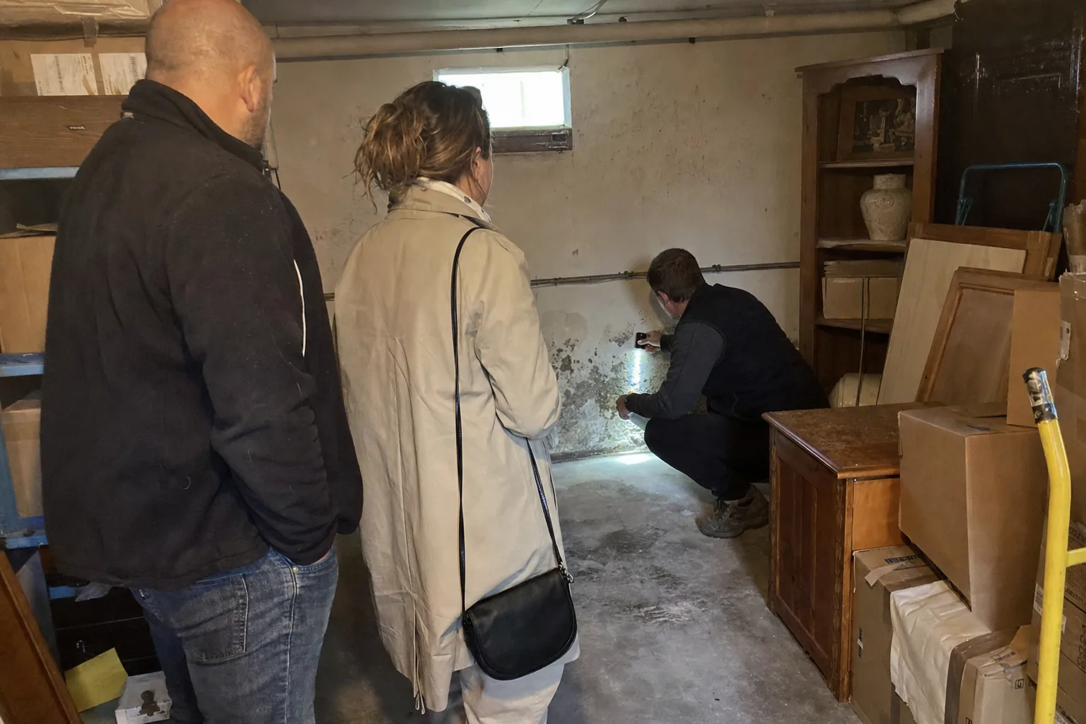 Expert bâtiment et acquéreurs examinant un mur de sous-sol à la lampe torche
