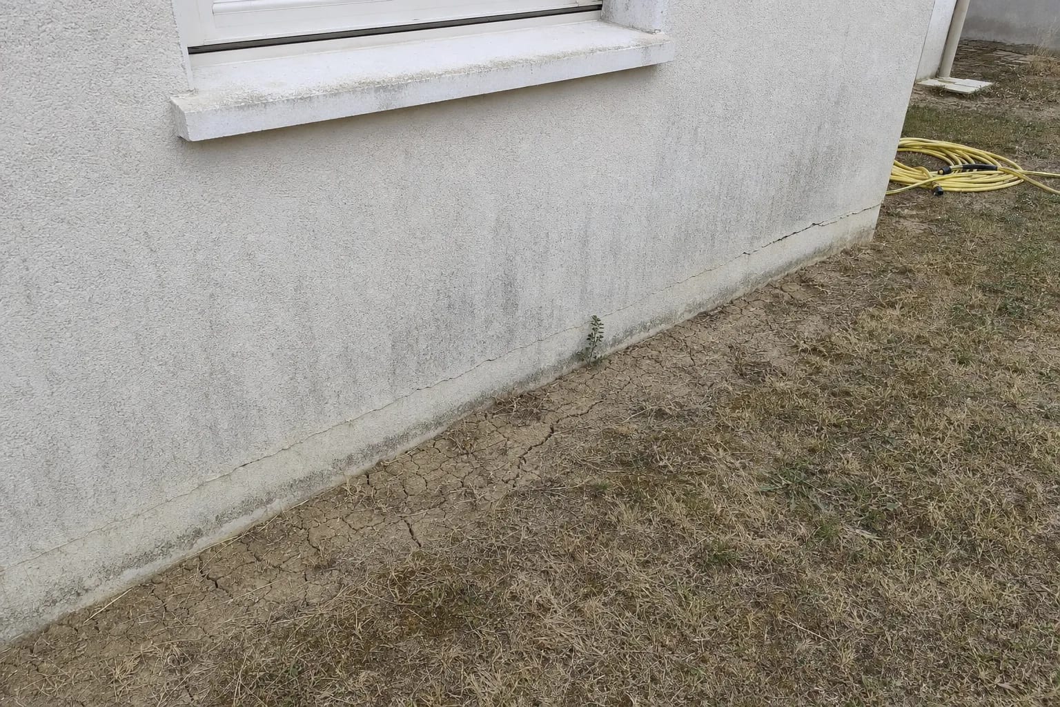 Sol argileux desséché et craquelé au pied de la façade d'un pavillon