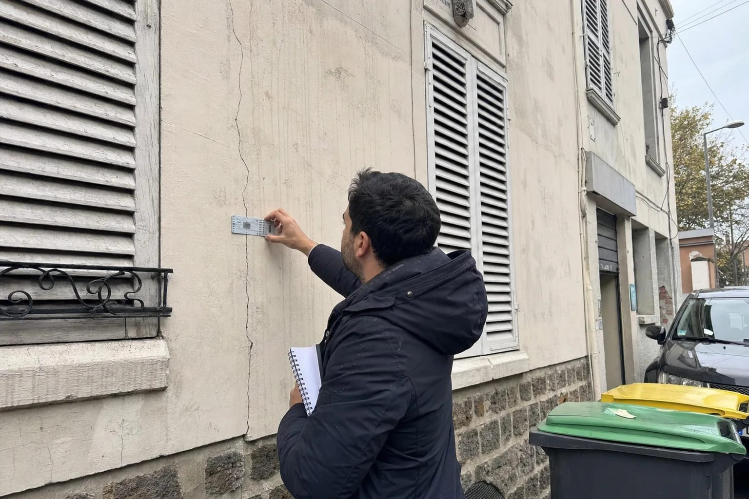Expert bâtiment examinant la façade fissurée d'un immeuble francilien