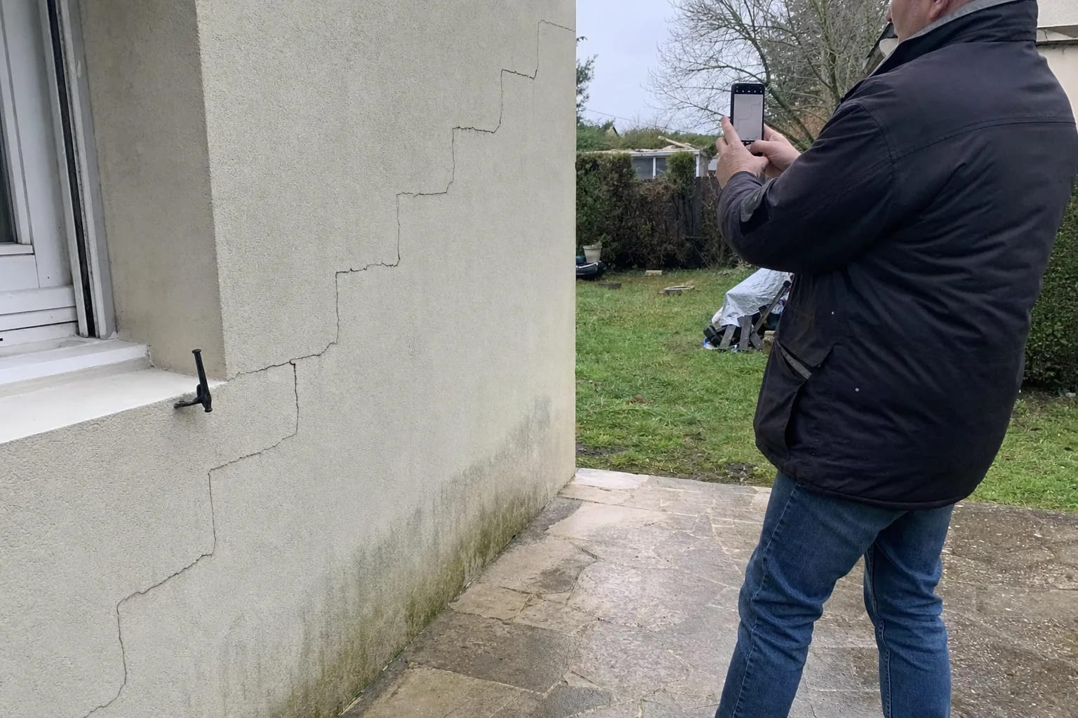 Main photographiant avec un smartphone une fissure en escalier sur un mur